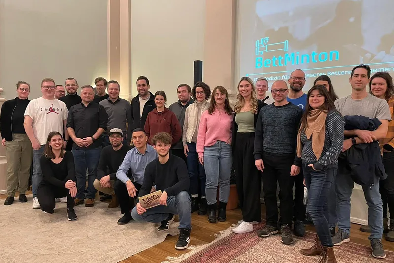 Gruppenbild der Pullerparty mit BettMinton, eine große Runde vor der Leinwand mit dem Logo von BettMinton