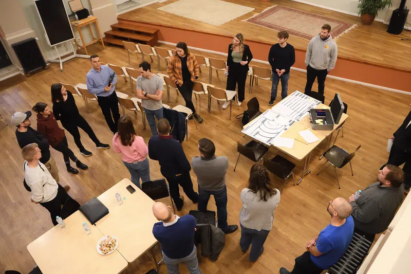 Blick von oben auf die Runde, die im Saal um einen Tisch mit Arbeitsblättern steht