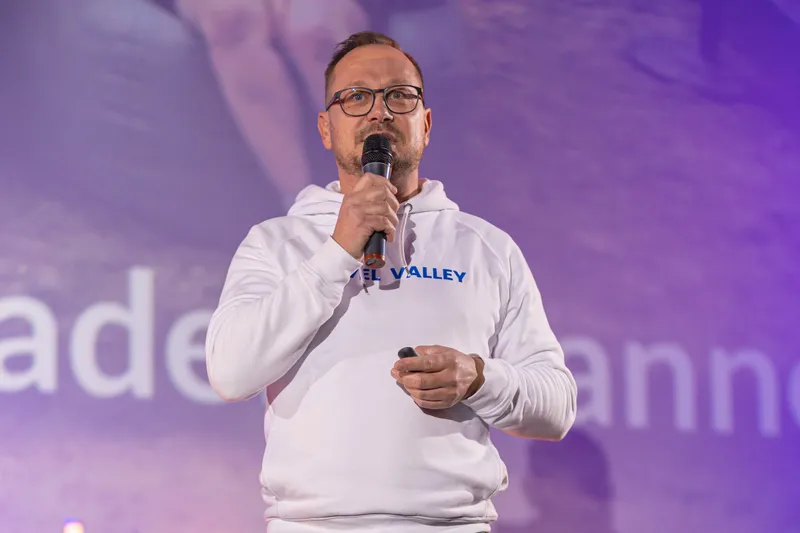 Ein Mann im weißen Havel-Valley-Pullover spricht mit Mikrofon auf der Bühne