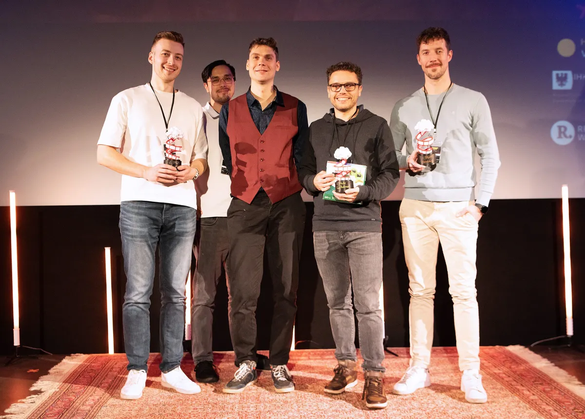 Gruppenbild auf der Bühne, drei Platzierte mit ihren Pokalen, dazwischen zwei weitere Personen